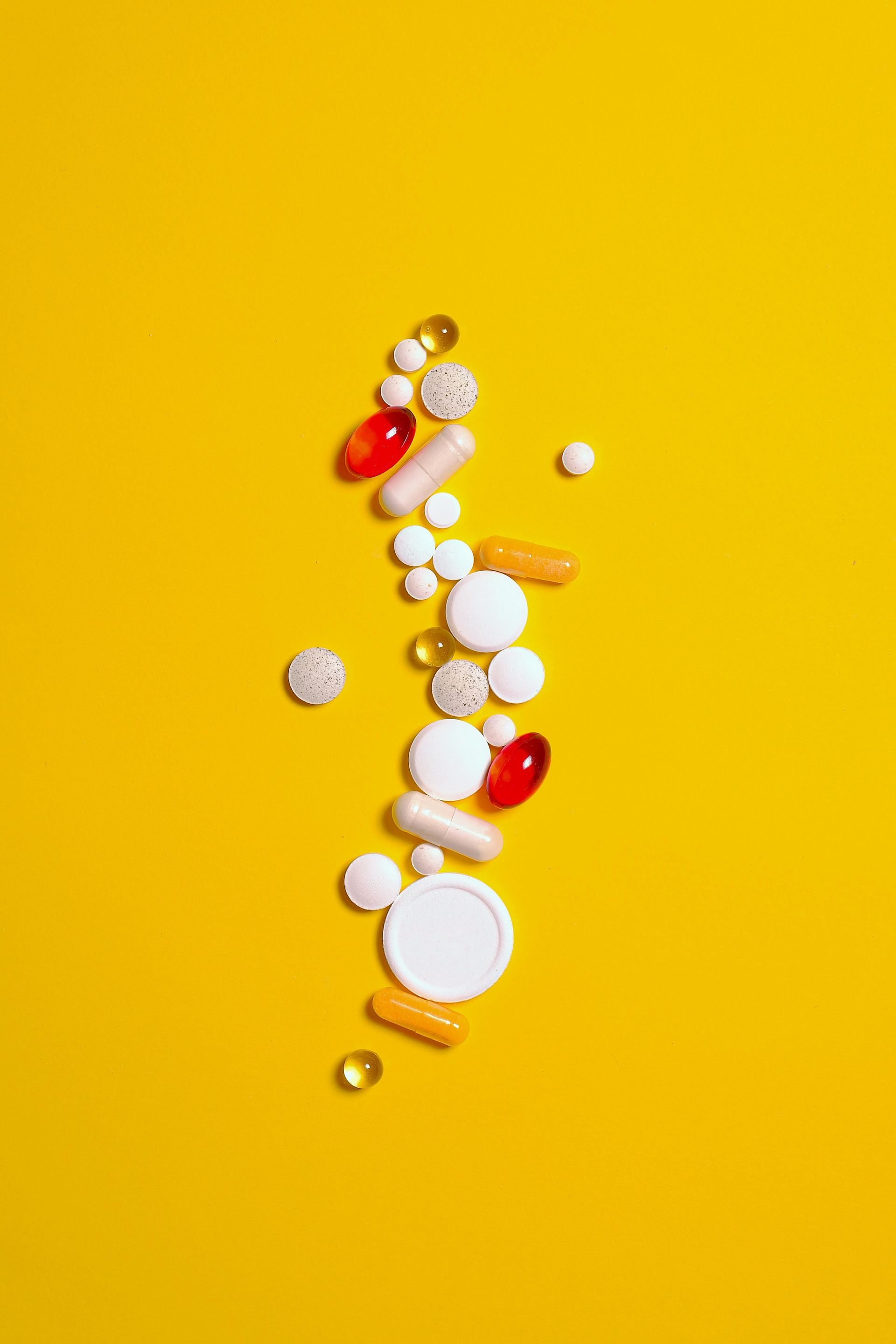 Auf gelbem Hintergrund sind viele verschiedene Pillenarten abgebildet.