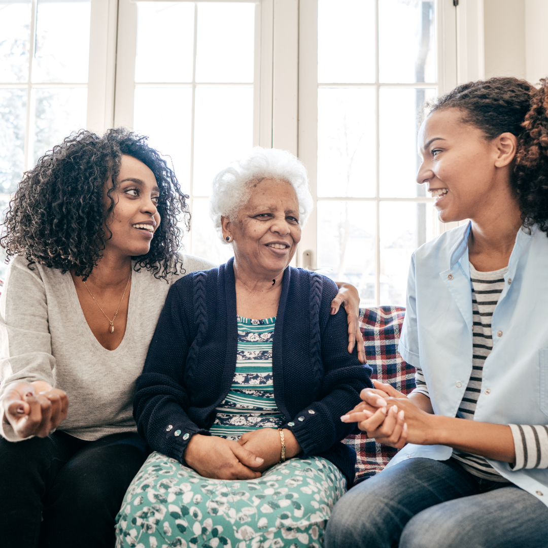 Three women on a couch, one elderly, two younger, smiling and talking.