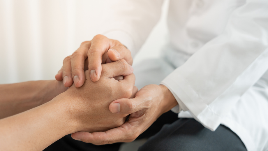 Doctor holding a patient's hand, offering comfort and support. The scene has a soft