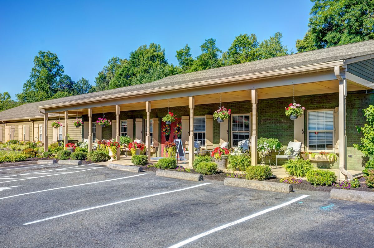 A motel with a long porch and a parking lot in front of it.