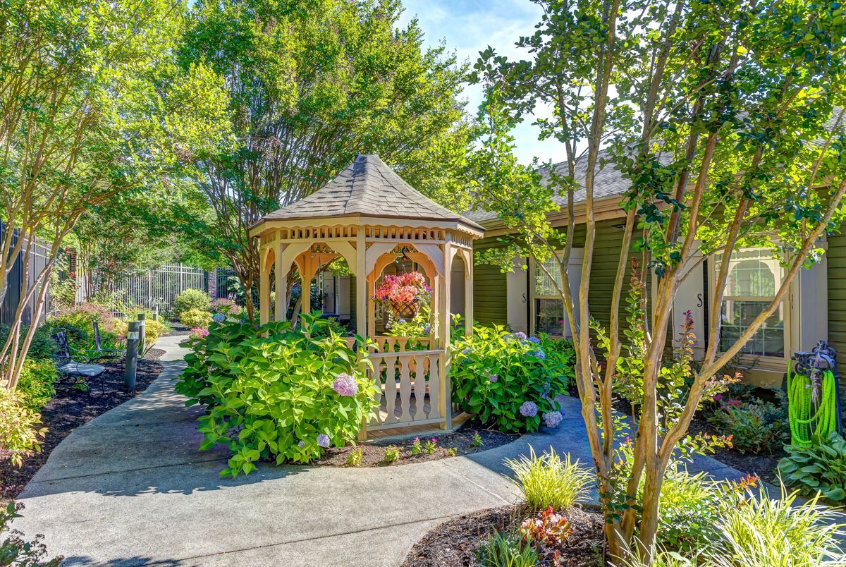 There is a gazebo in the middle of a garden surrounded by trees.