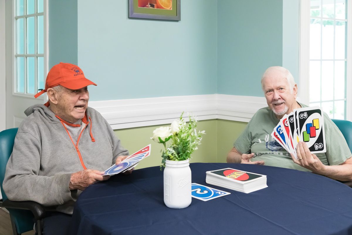 Two elderly men are sitting at a table playing uno cards.