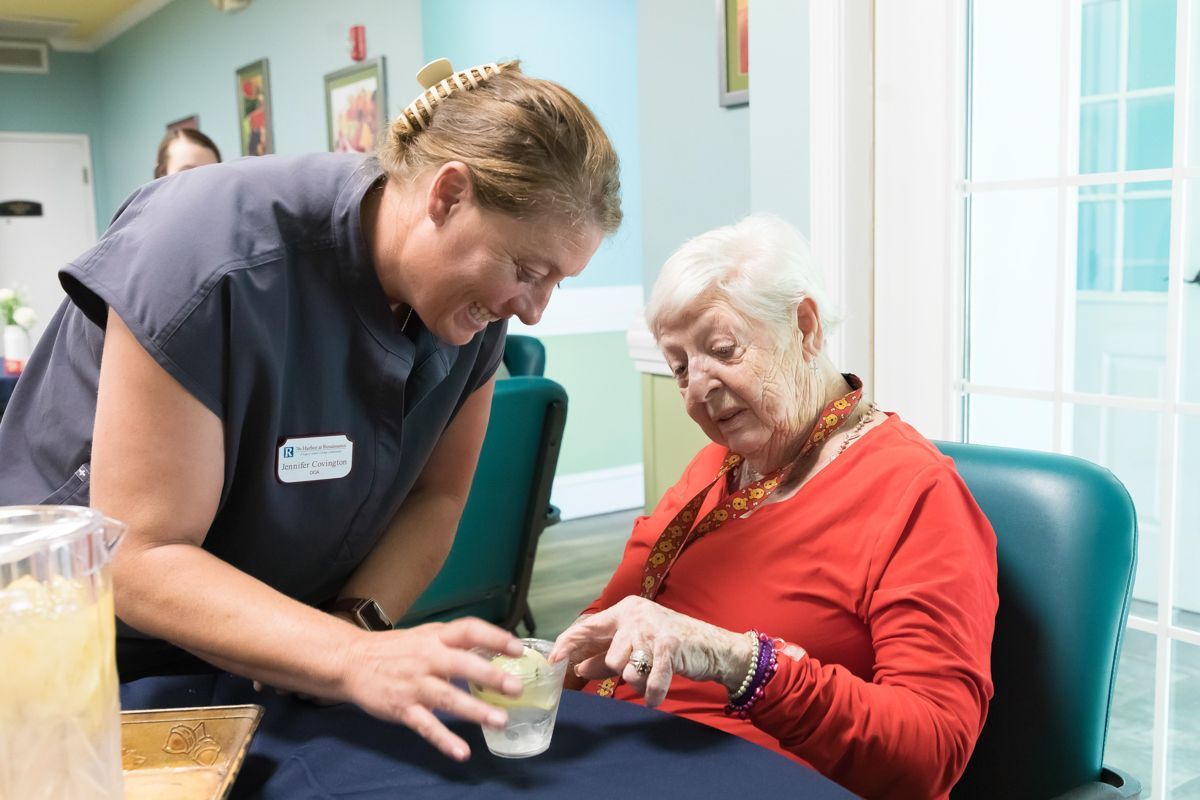 A nurse is giving an elderly woman a glass of water.