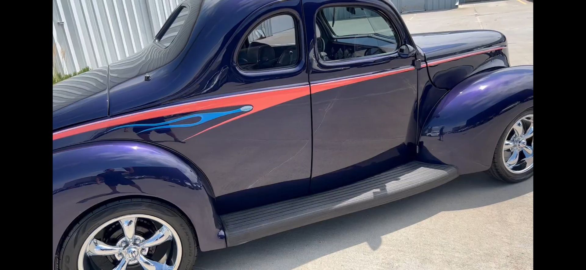 A purple car with red and blue stripes is parked on the side of the road.