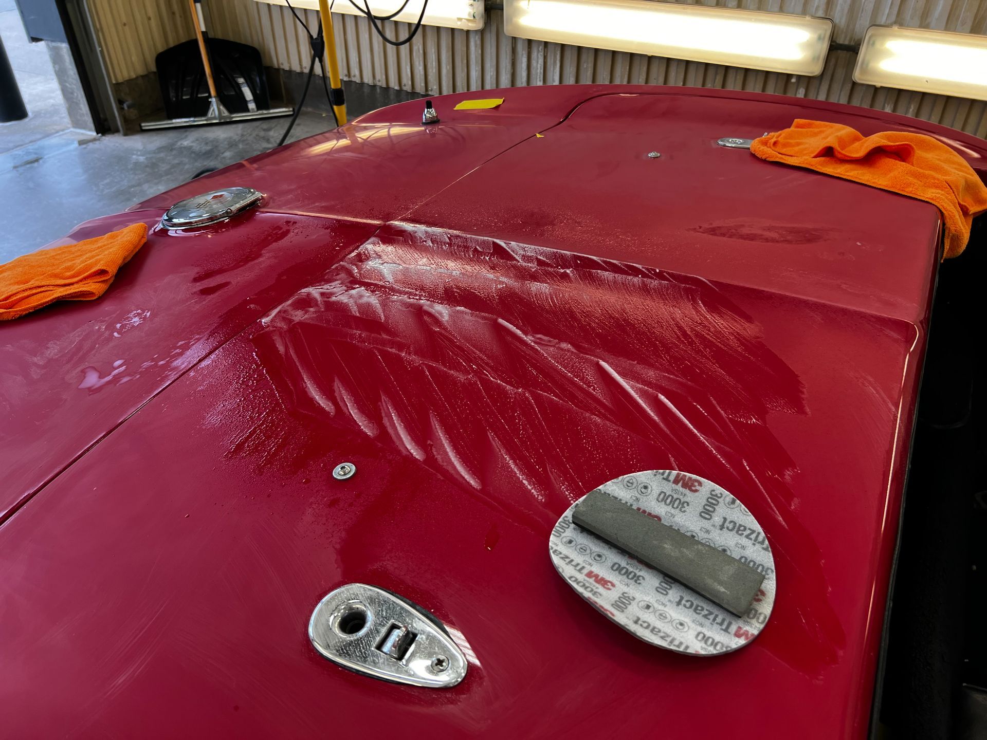 The hood of a red car is being worked on in a garage.