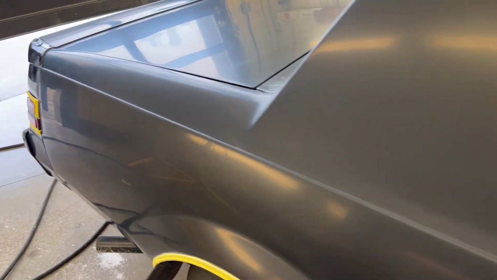 A gray car with a yellow stripe on the side is sitting in a garage.