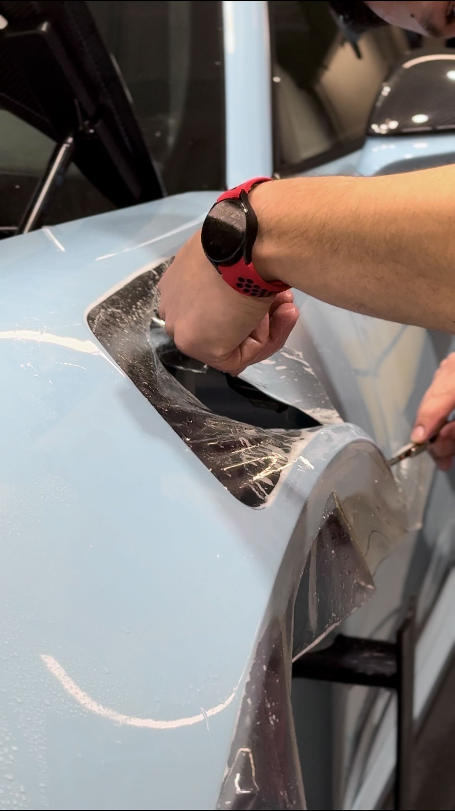 A person wearing a watch is wrapping a car with plastic wrap