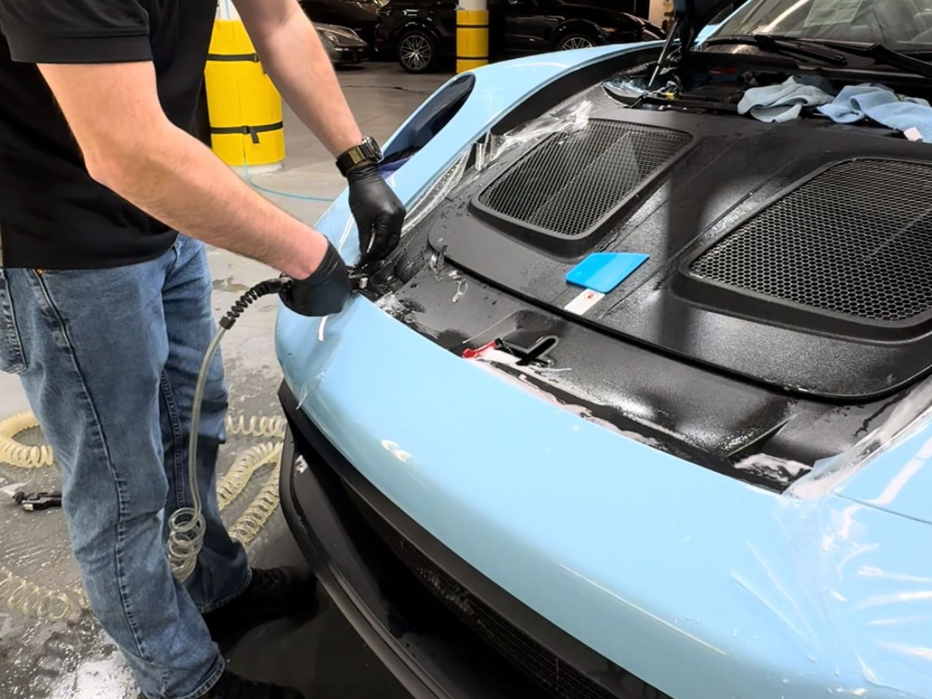 A man is cleaning the front of a car with a hose.