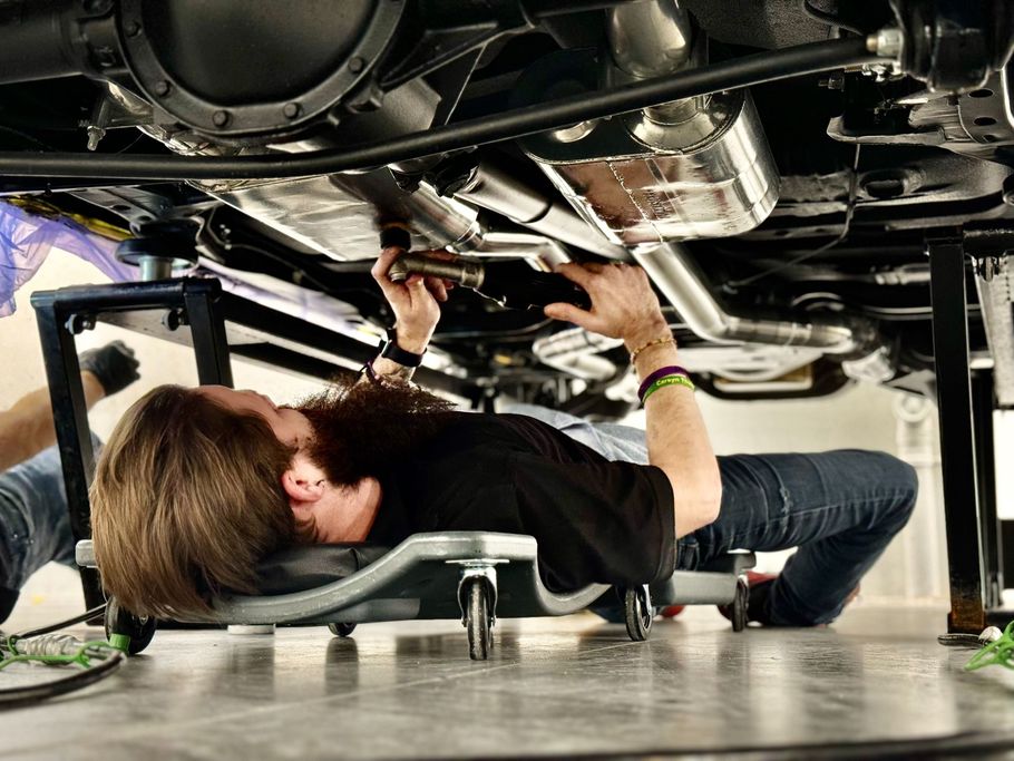 A man is laying on a bed under a car working on it.