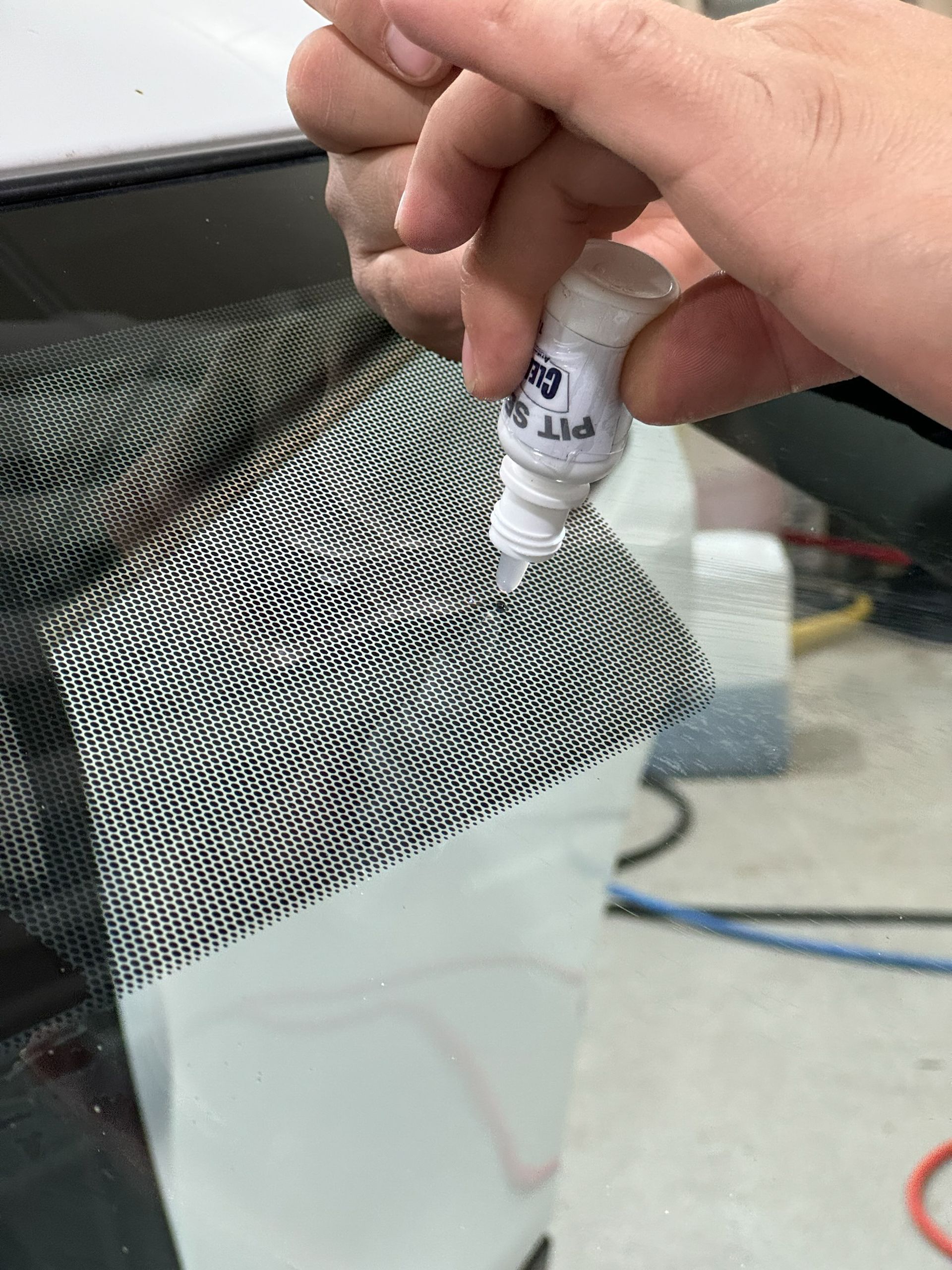 A person is holding a bottle of glue over a piece of mesh.