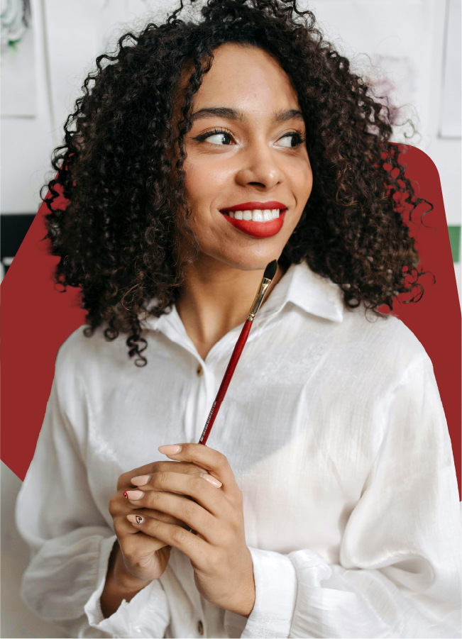 A woman with curly hair is holding a brush and smiling.