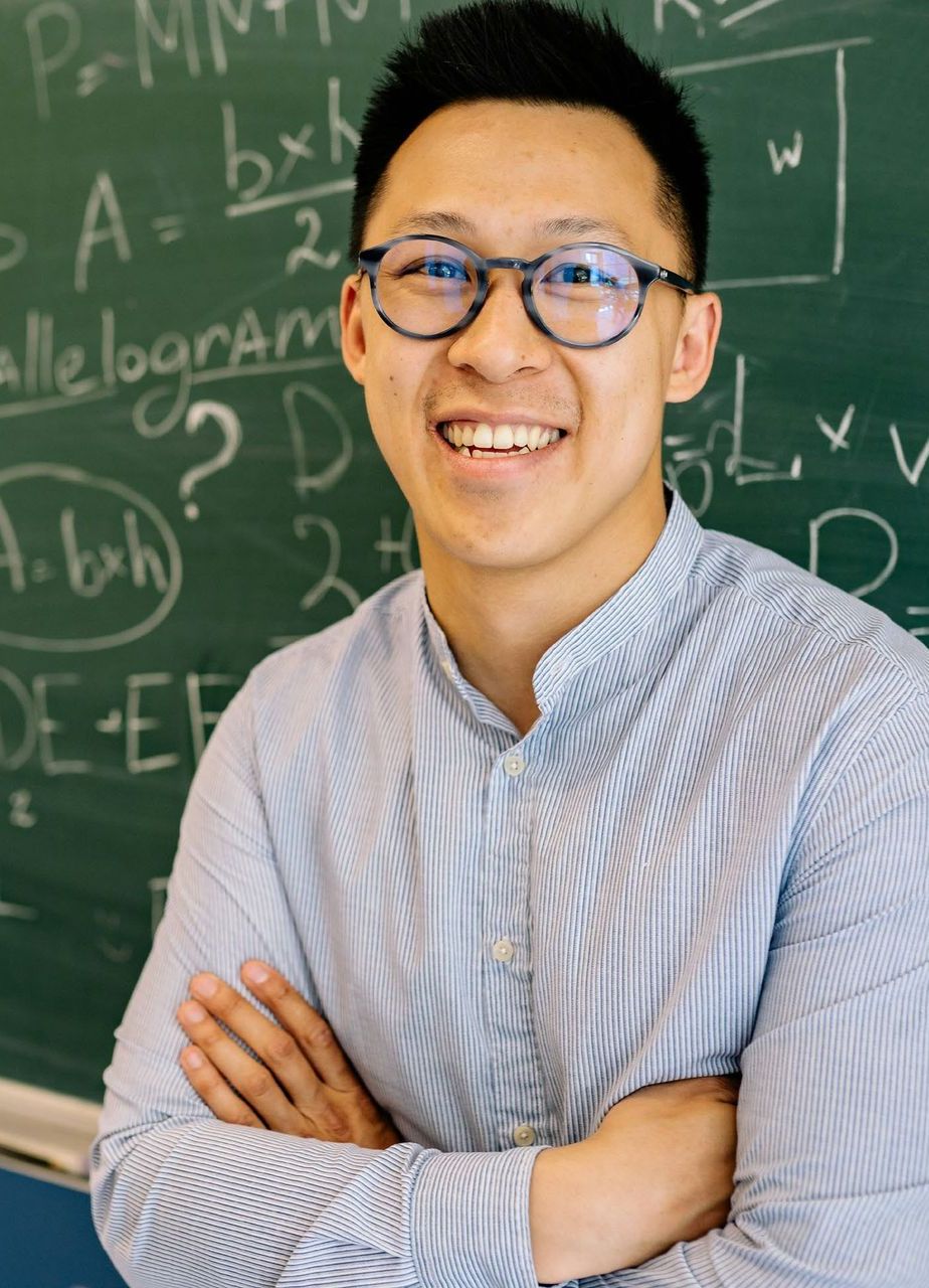 A man wearing glasses stands in front of a blackboard