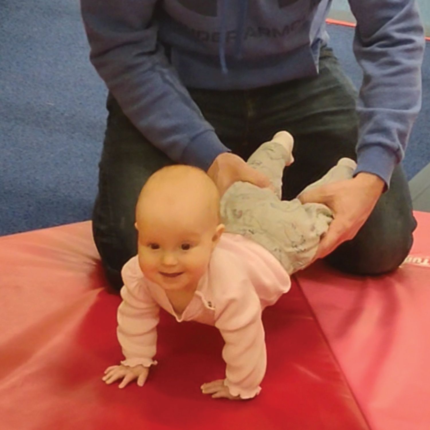 A baby in a pink shirt is crawling on a red mat