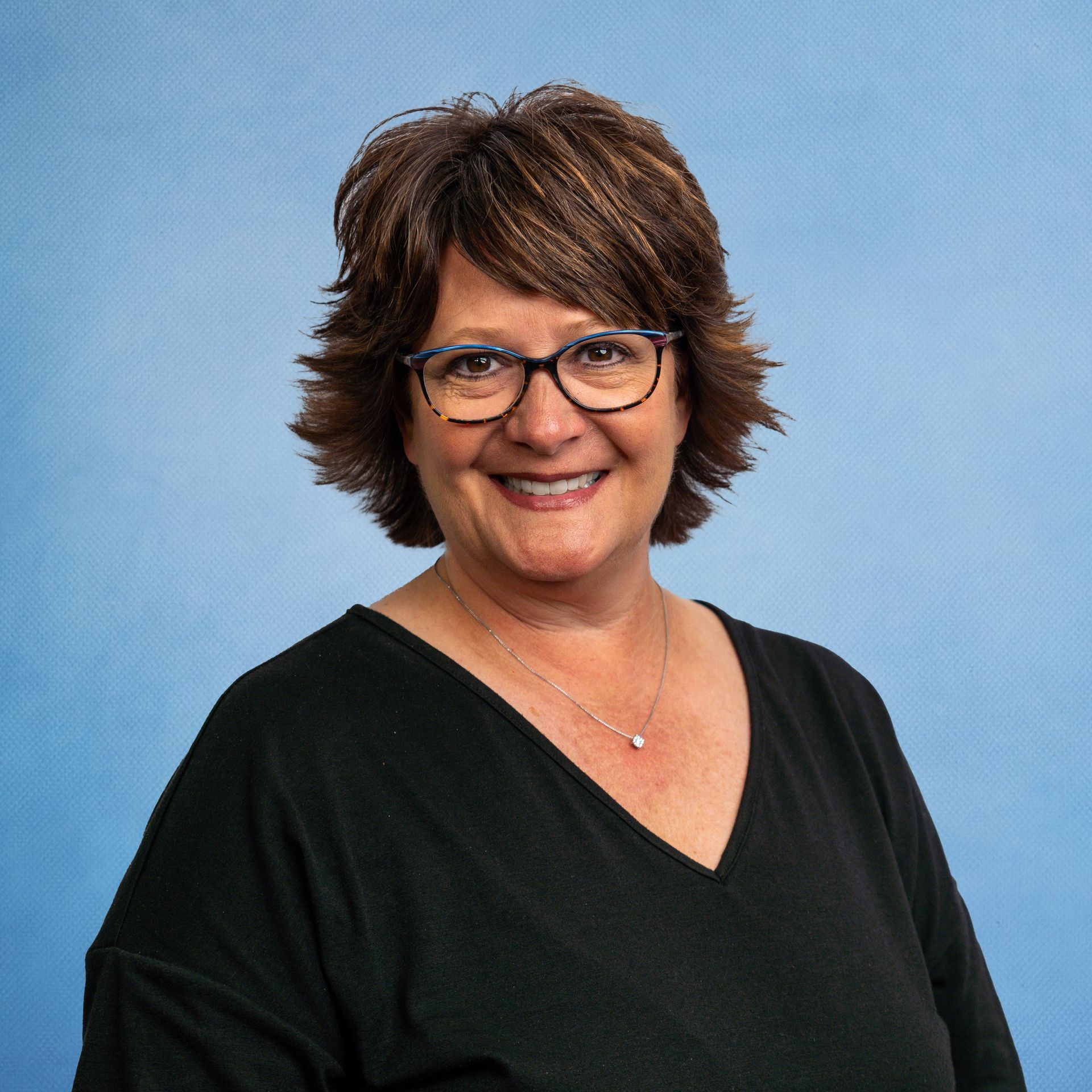 A woman wearing glasses and a black shirt is smiling for the camera.