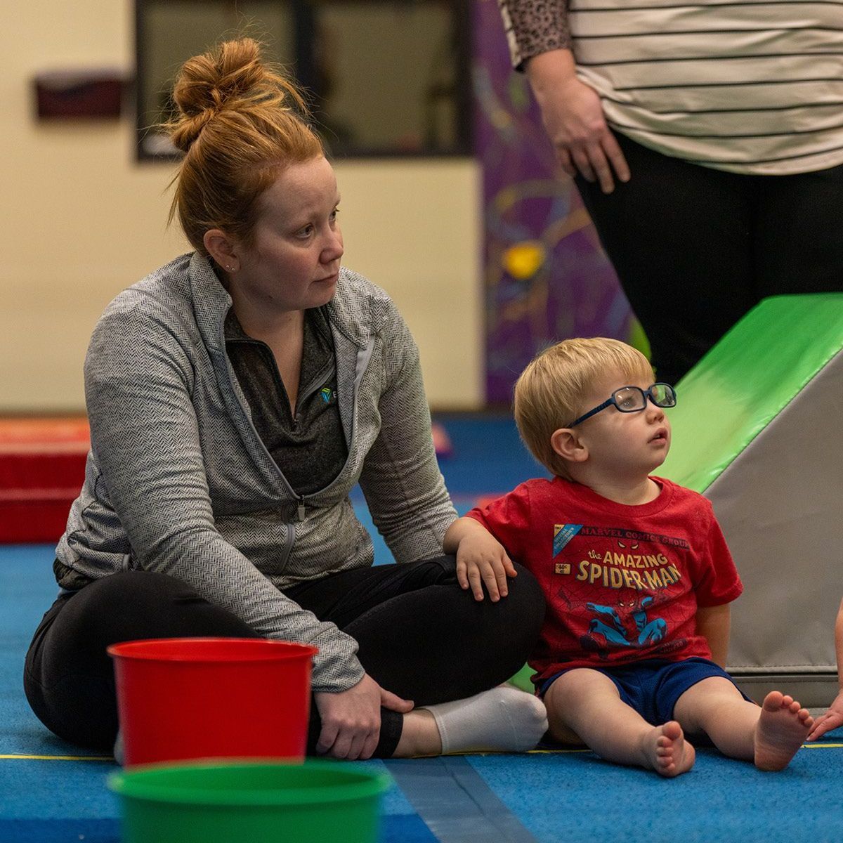 A man is kneeling next to a little boy holding a bar in a gym