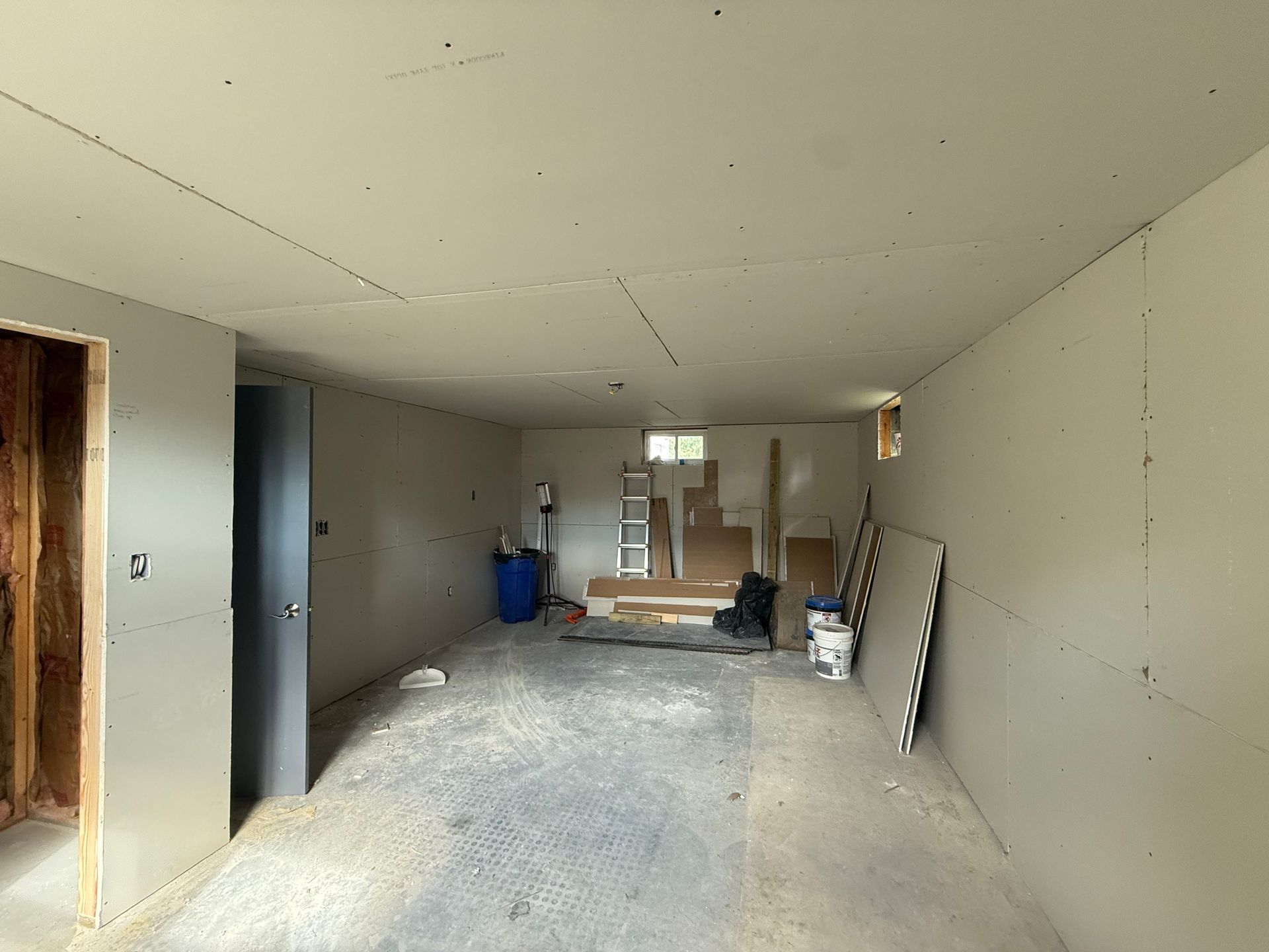 Basement under renovation. Drywall on walls and ceiling, concrete floor, doorway, window, building materials.