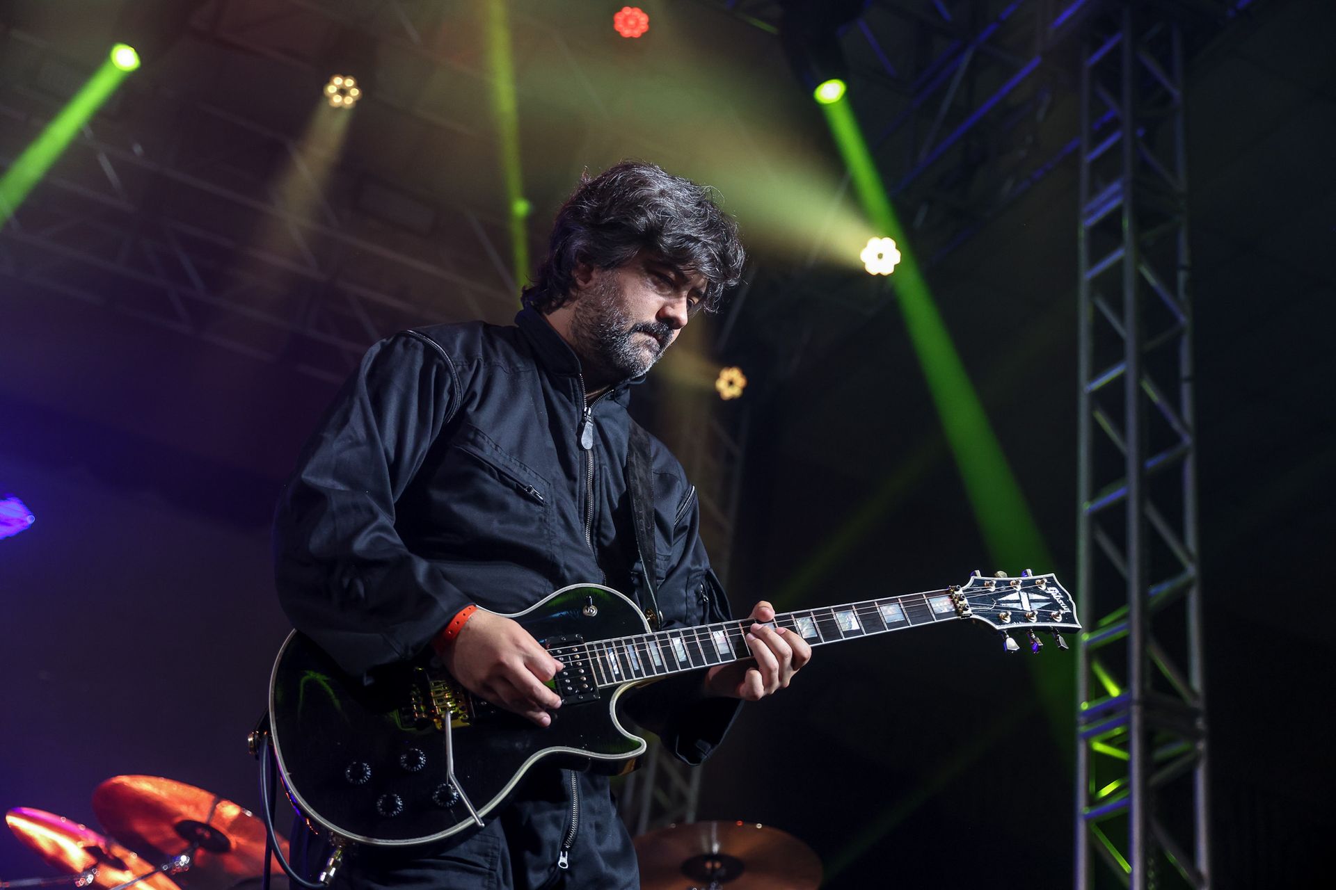 Uma pessoa tocando guitarra elétrica preta no palco sob holofotes verdes.