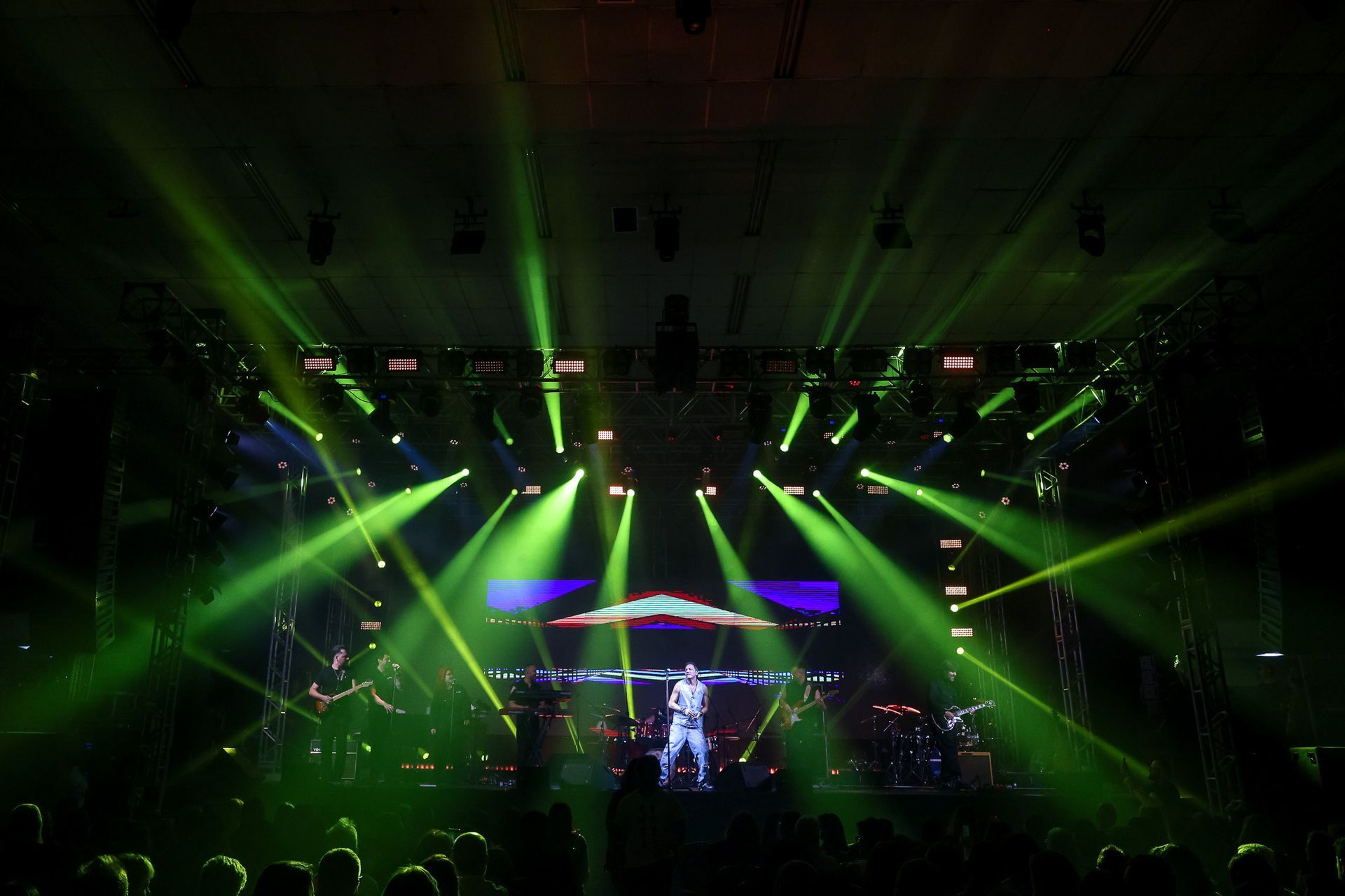 Um artista está em um palco banhado por holofotes verdes brilhantes e vibrantes, com uma grande tela ao fundo.