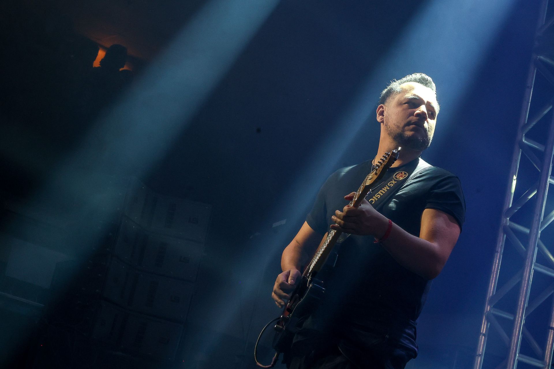 Um músico toca guitarra elétrica sob luzes de palco brilhantes em uma casa de shows escura.