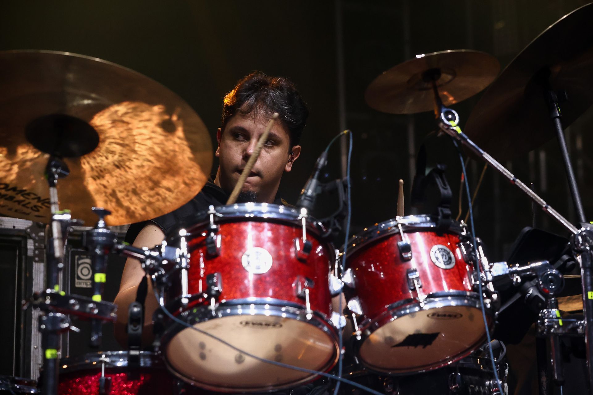 Um baterista toca uma bateria vermelha com pratos em um palco sob iluminação de palco.