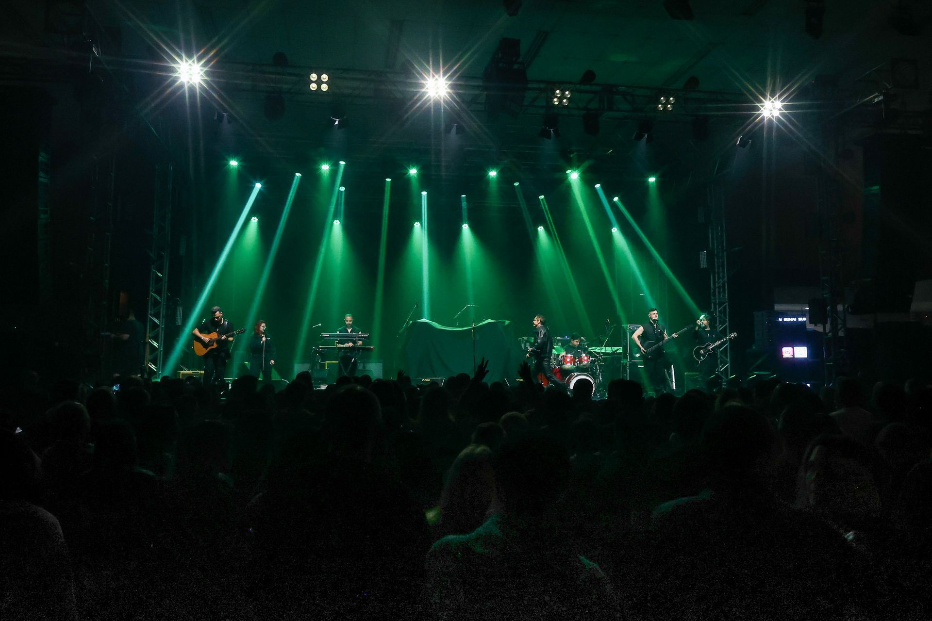 Uma banda se apresenta em um palco banhado por luzes verdes brilhantes diante de uma plateia em silhueta