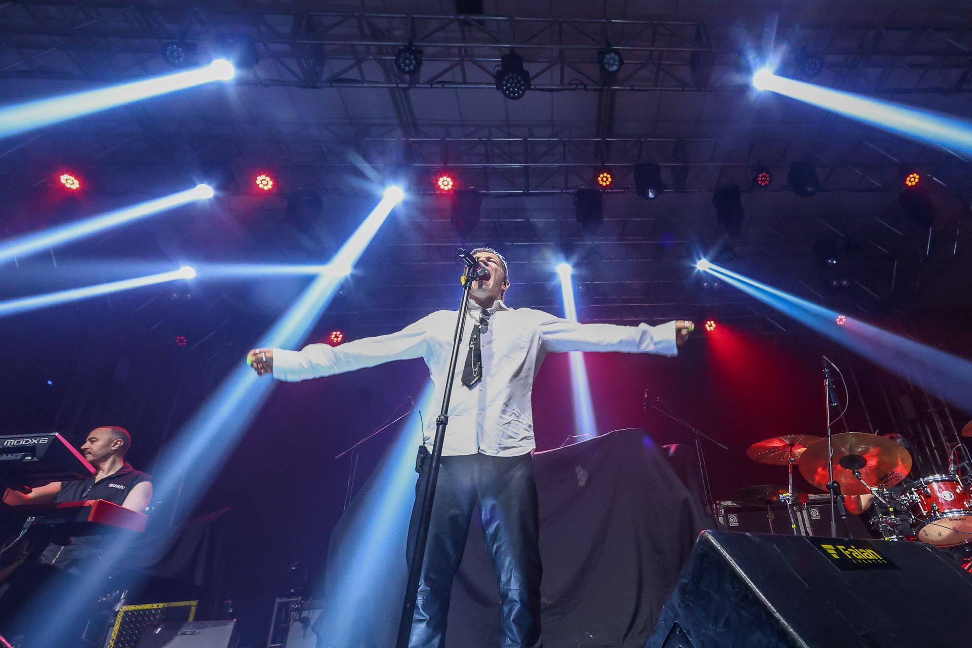 Um artista com os braços estendidos está no centro do palco sob holofotes azuis brilhantes durante um concerto.