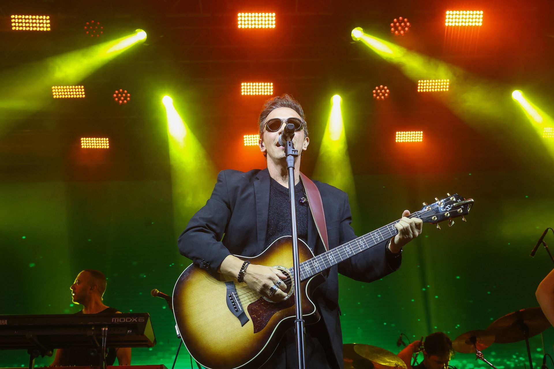 Um artista cantando e tocando violão no palco sob holofotes amarelos brilhantes.