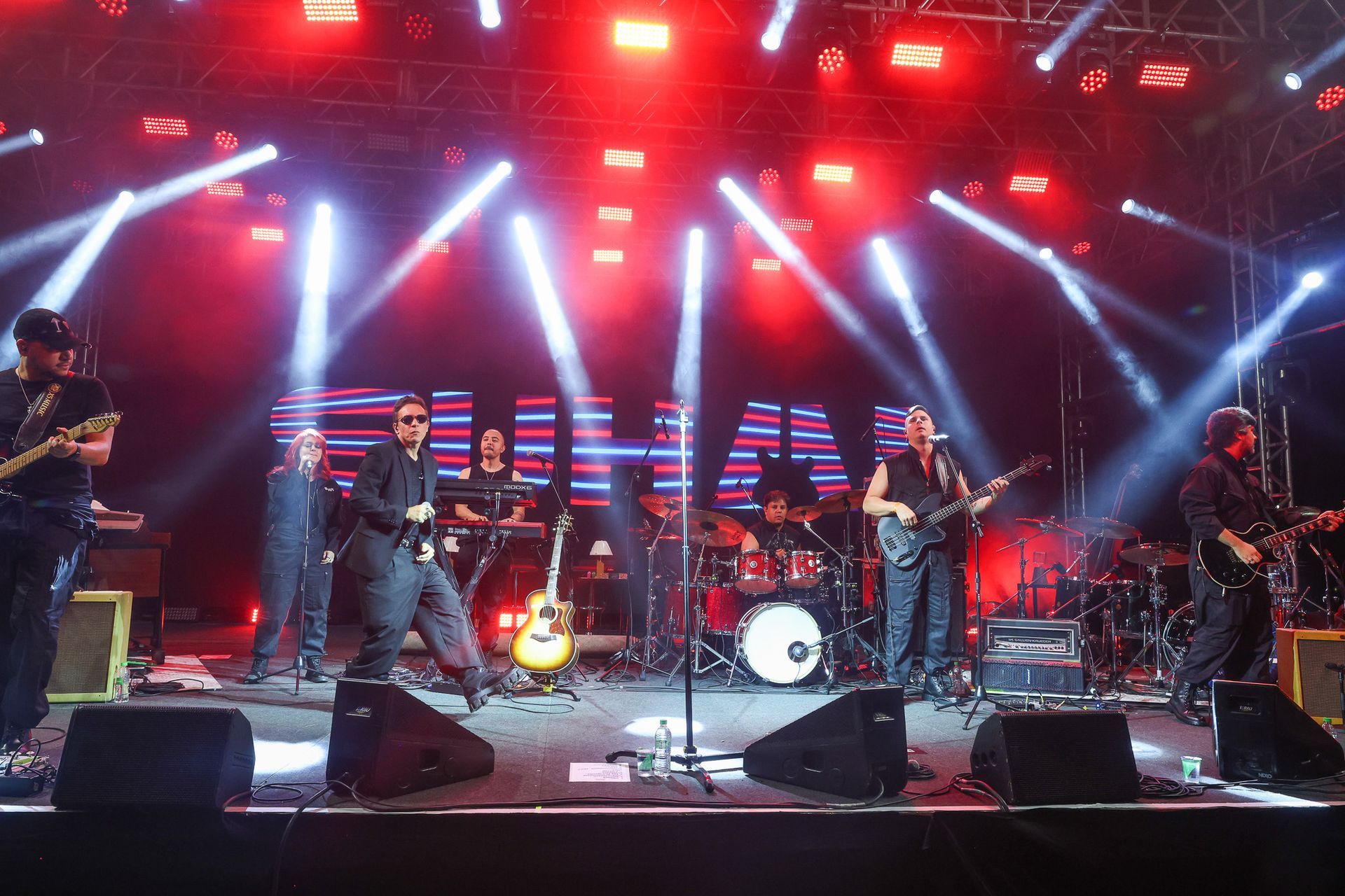 Uma banda de rock se apresenta com músicos tocando guitarras, bateria e teclados.