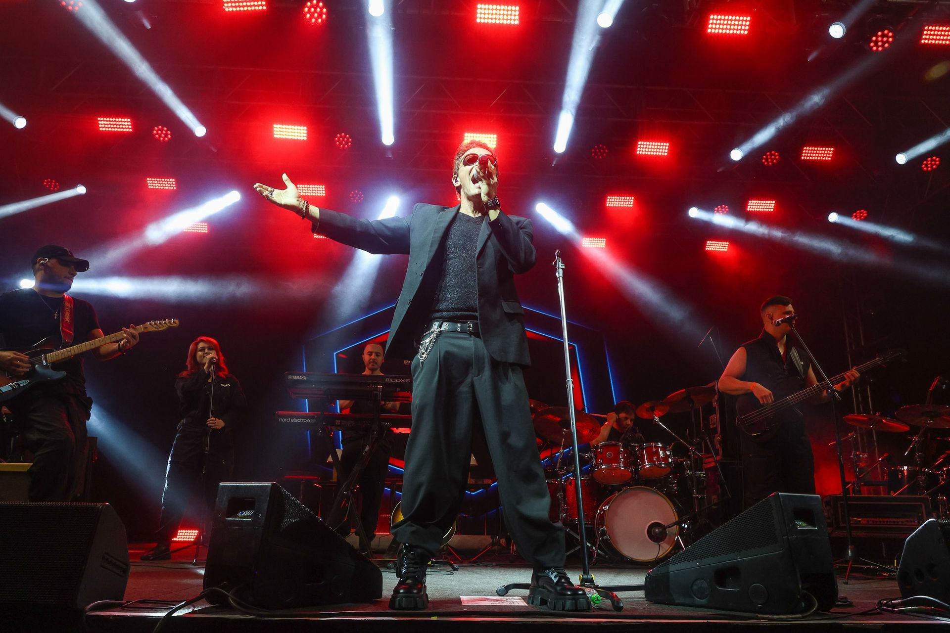 O vocalista principal se apresenta em um palco com uma banda ao vivo, iluminado por holofotes