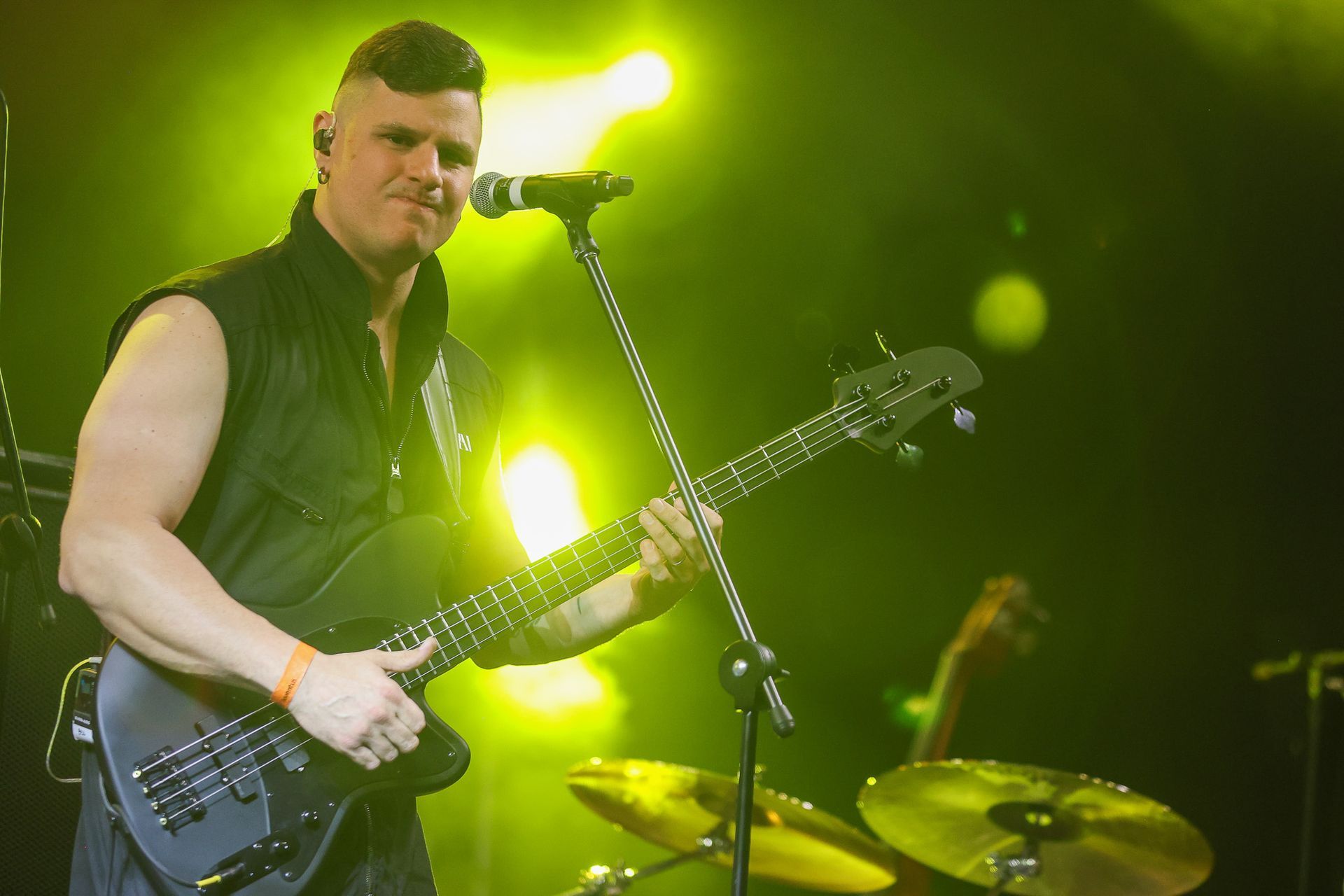 Um músico tocando um baixo preto em um palco banhado por holofotes amarelos brilhantes.
