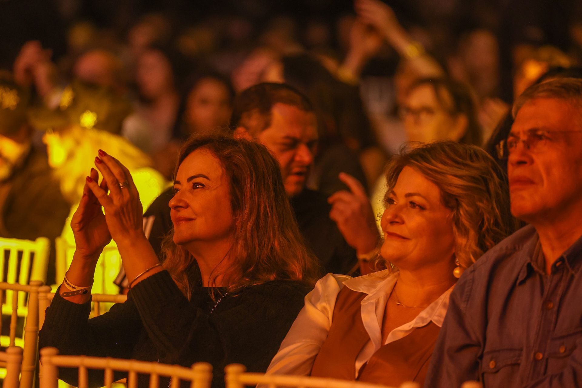 Os espectadores sentam-se; uma pessoa aplaude, enquanto as outras assistem atentamente, sentadas em um ambiente interno.