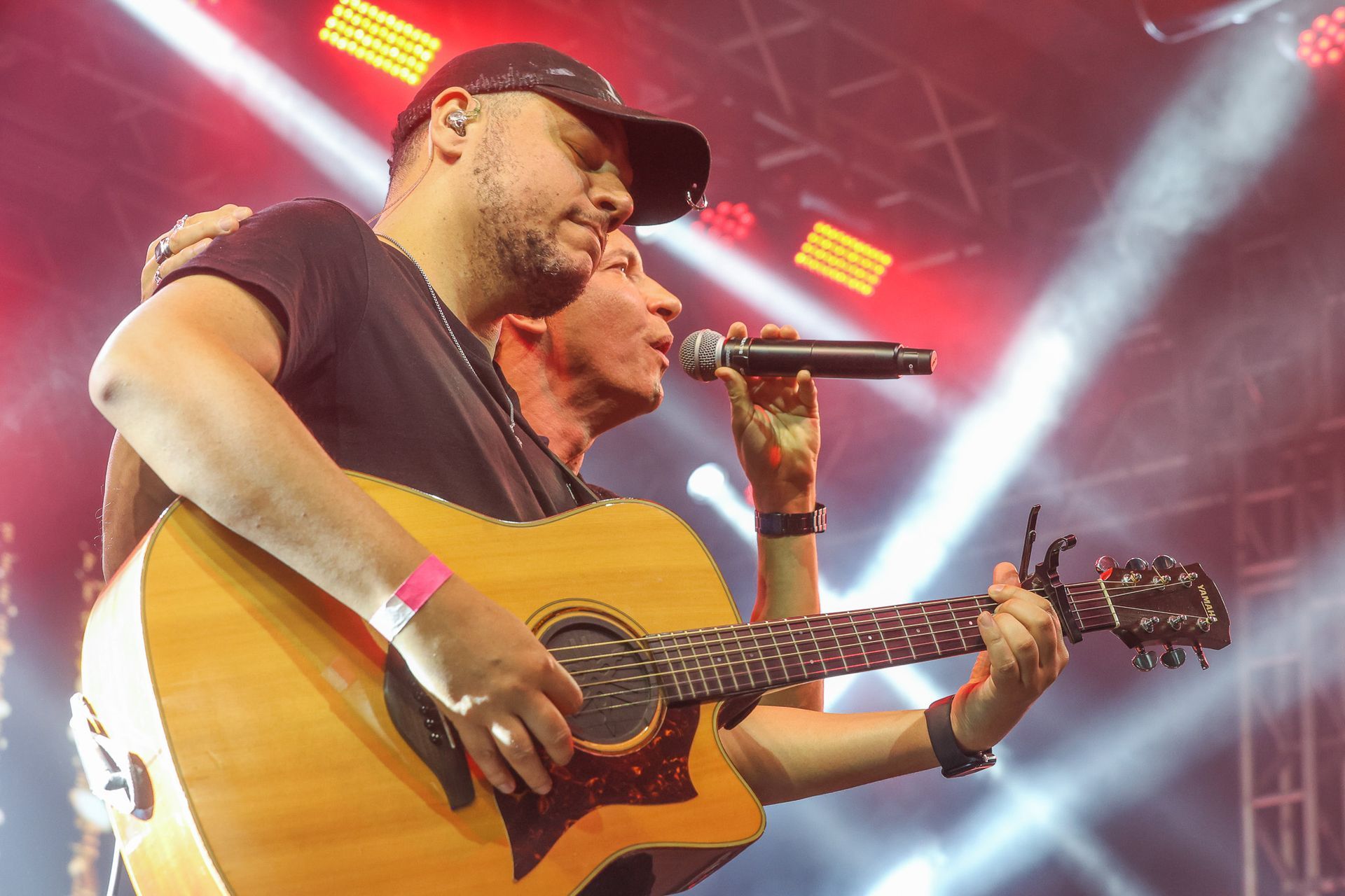 Dois músicos se apresentando no palco; um toca violão enquanto o outro canta ao microfone.