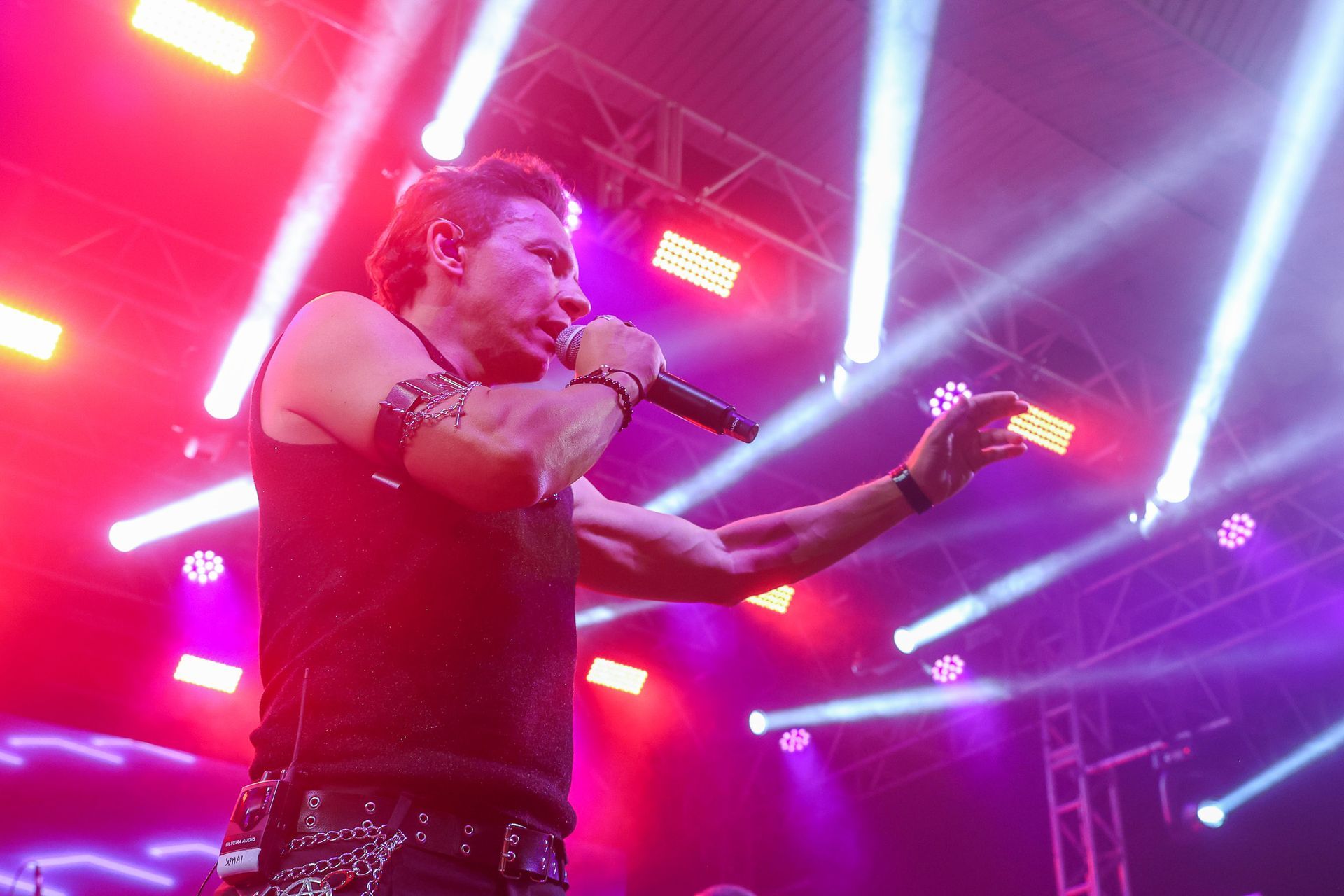 Um artista canta em um microfone em um palco repleto de luzes brilhantes e coloridas e uma névoa roxa.