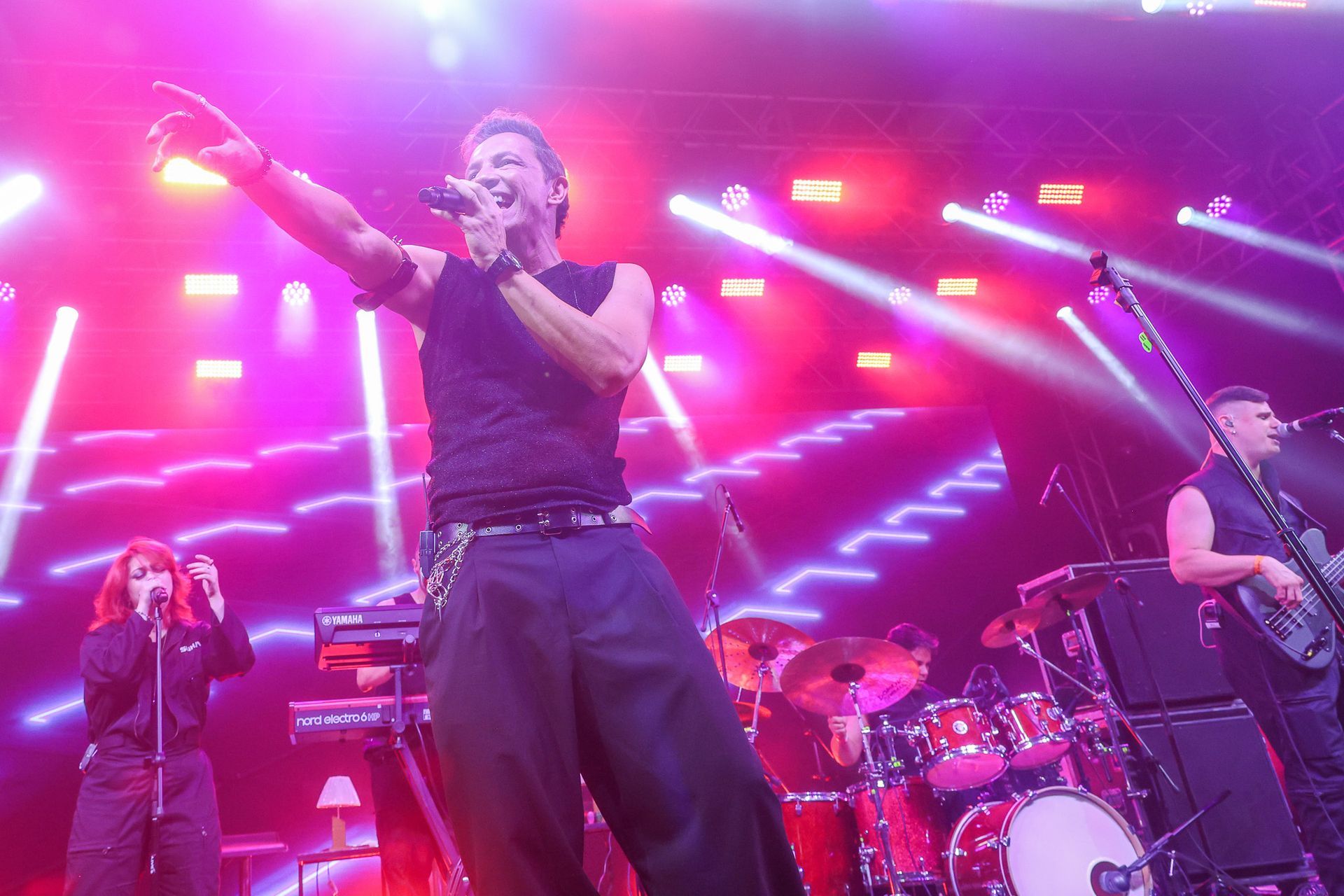 Uma banda se apresenta em um palco de shows brilhantemente iluminado com luzes e feixes de luz magenta