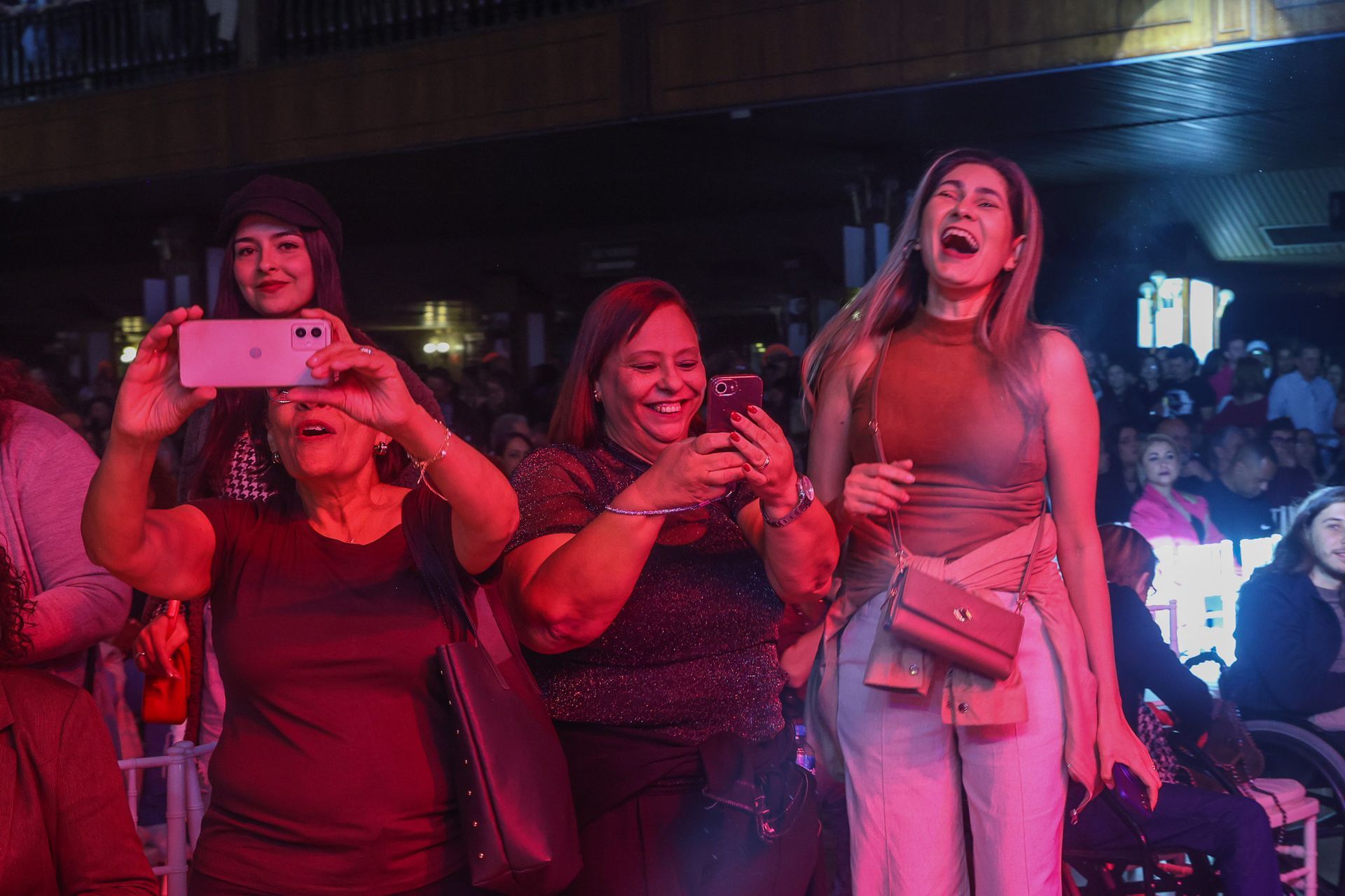 Três pessoas, duas filmando com smartphones enquanto a terceira ri com os braços erguidos.