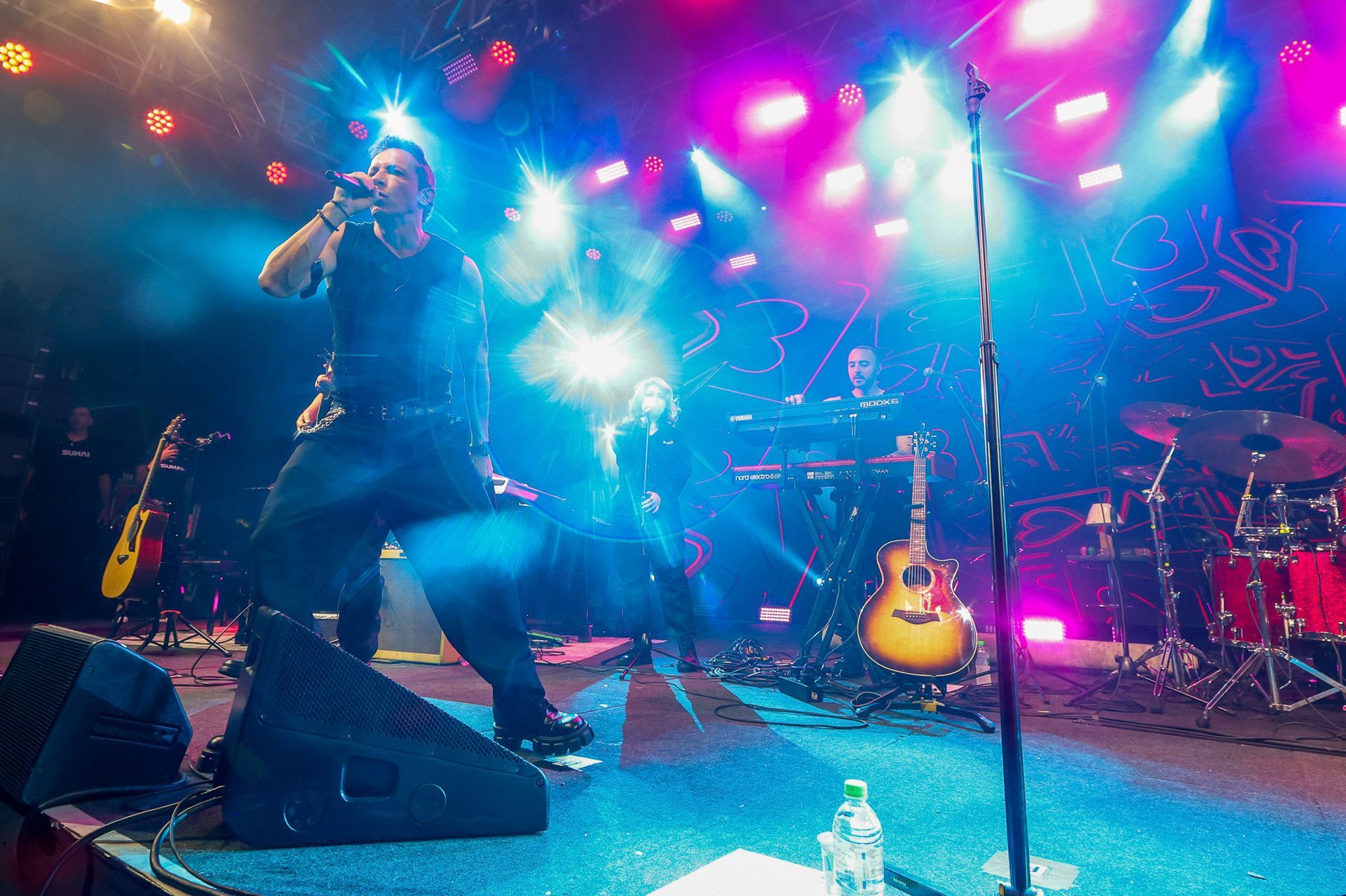 Uma banda de rock se apresentando em um palco iluminado por holofotes vibrantes em tons de azul e roxo.
