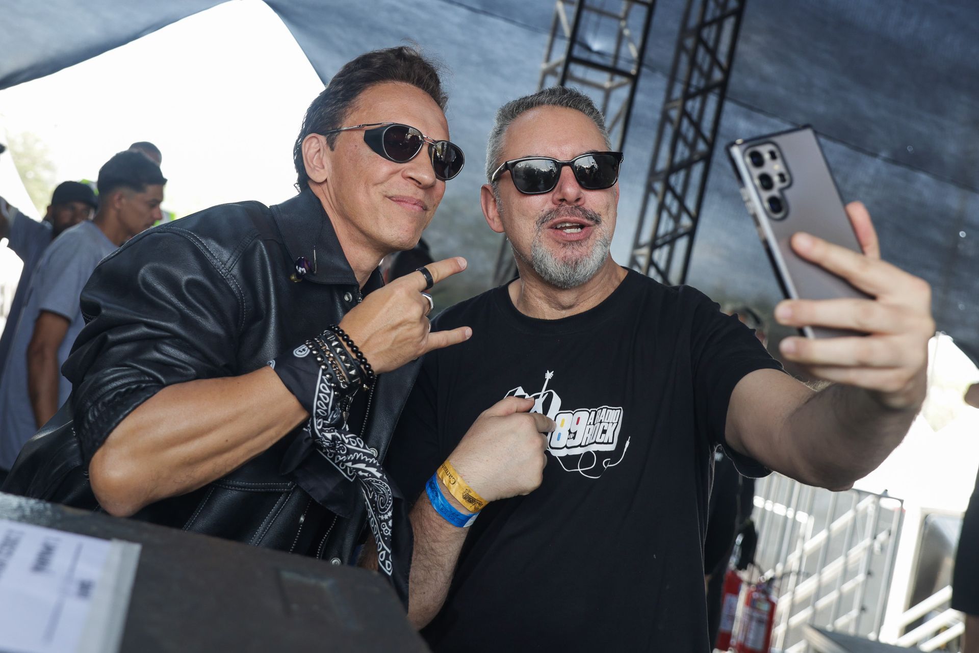 Dois homens de óculos escuros posando para uma selfie ao ar livre.