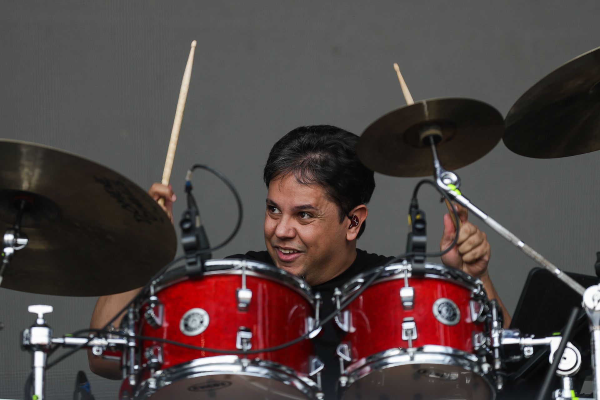 Um baterista sorridente toca uma bateria vermelha durante uma apresentação.