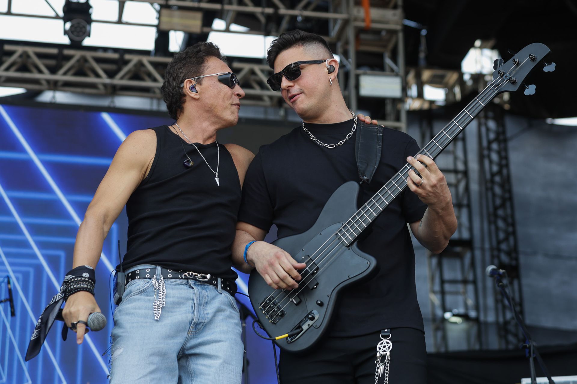 Dois artistas no palco: um cantando ao microfone, o outro tocando um baixo preto, olhando um para o outro.
