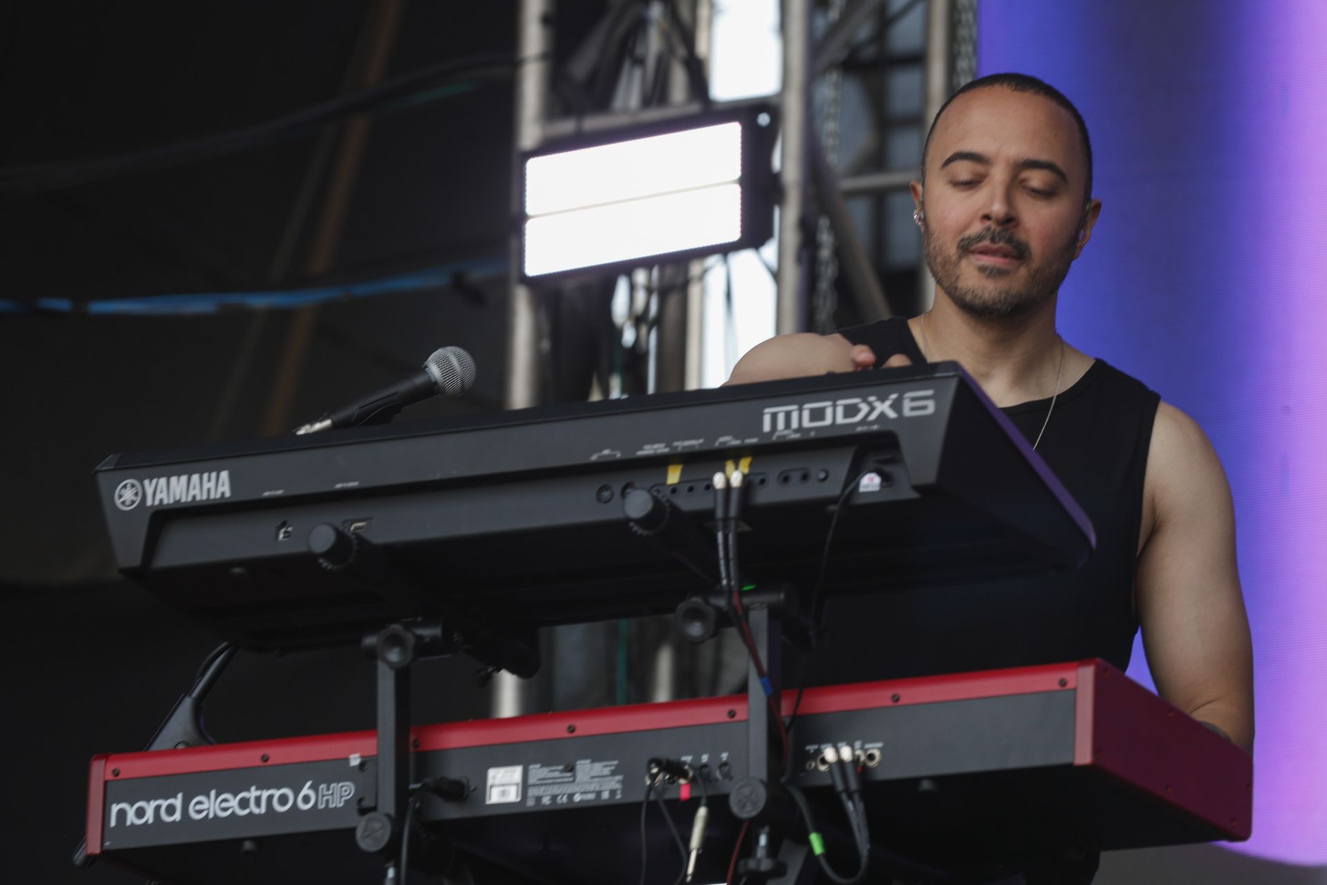 Um músico se apresentando no palco com um sintetizador Yamaha MODX6 empilhado acima de um teclado Nord Electro 6D vermelho.