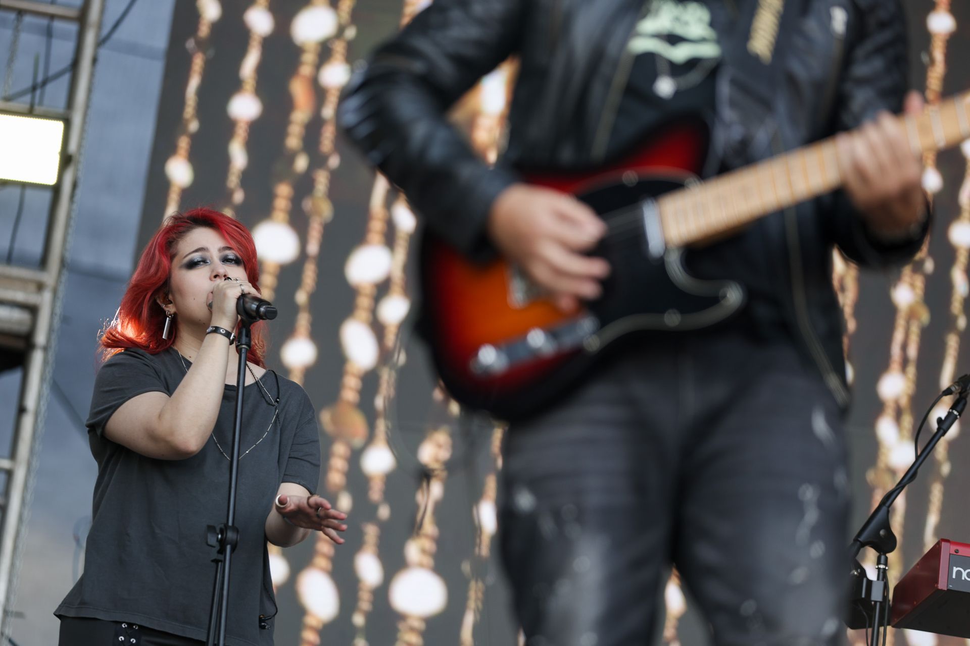 Uma cantora ruiva se apresenta ao microfone no palco, ao lado de um guitarrista que toca guitarra elétrica.