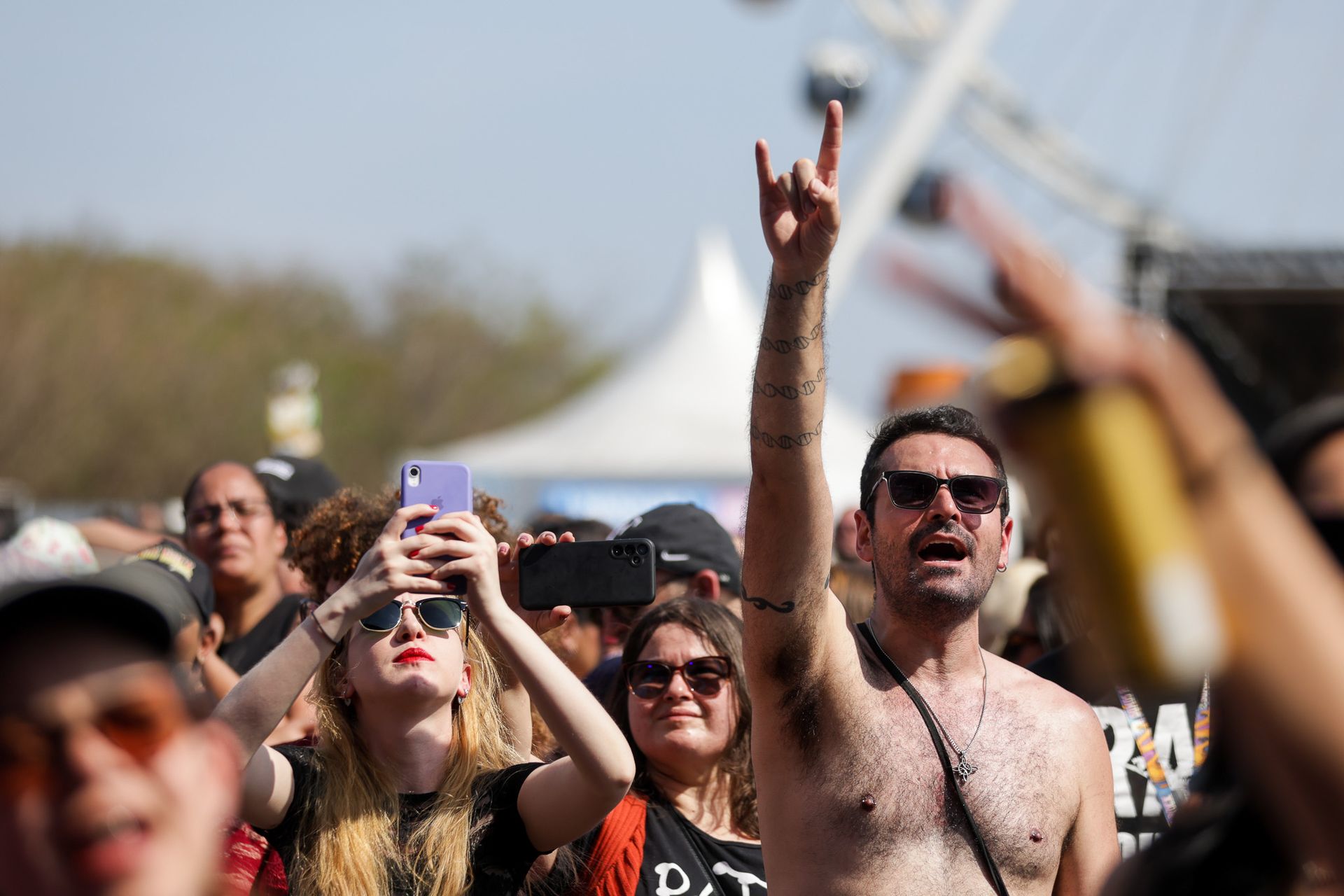 Uma multidão em um festival ao ar livre, com um homem sem camisa levantando a mão em sinal de apoio ao rock.