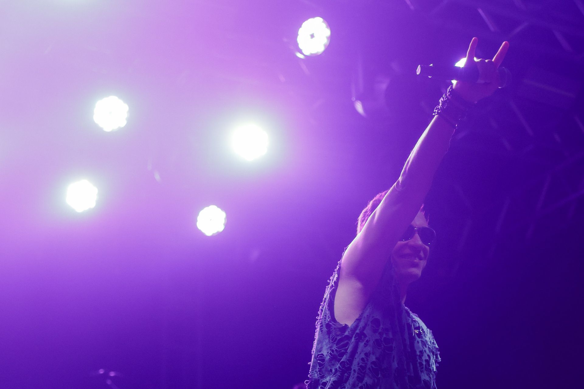 Um artista com o braço levantado sob luz roxa de palco.