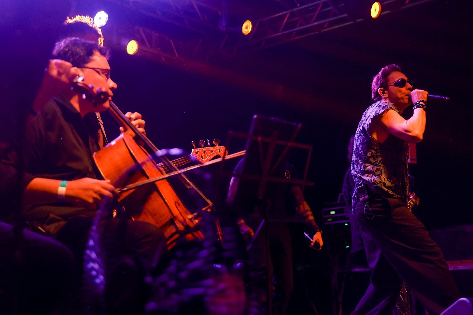 Violoncelista e cantor se apresentando no palco sob luzes de palco.