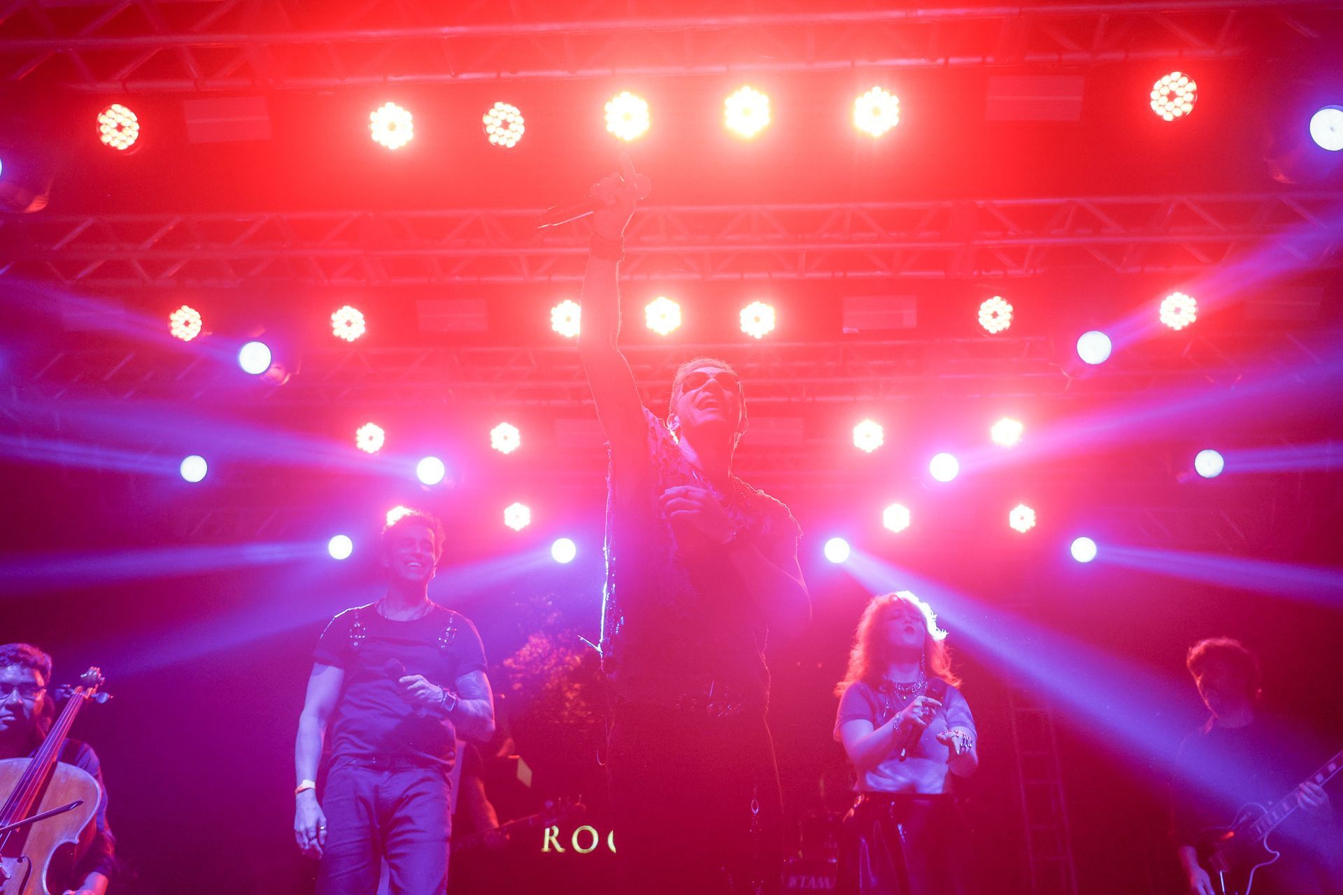Um artista no palco, iluminado por luzes vermelhas, cantando em um microfone.