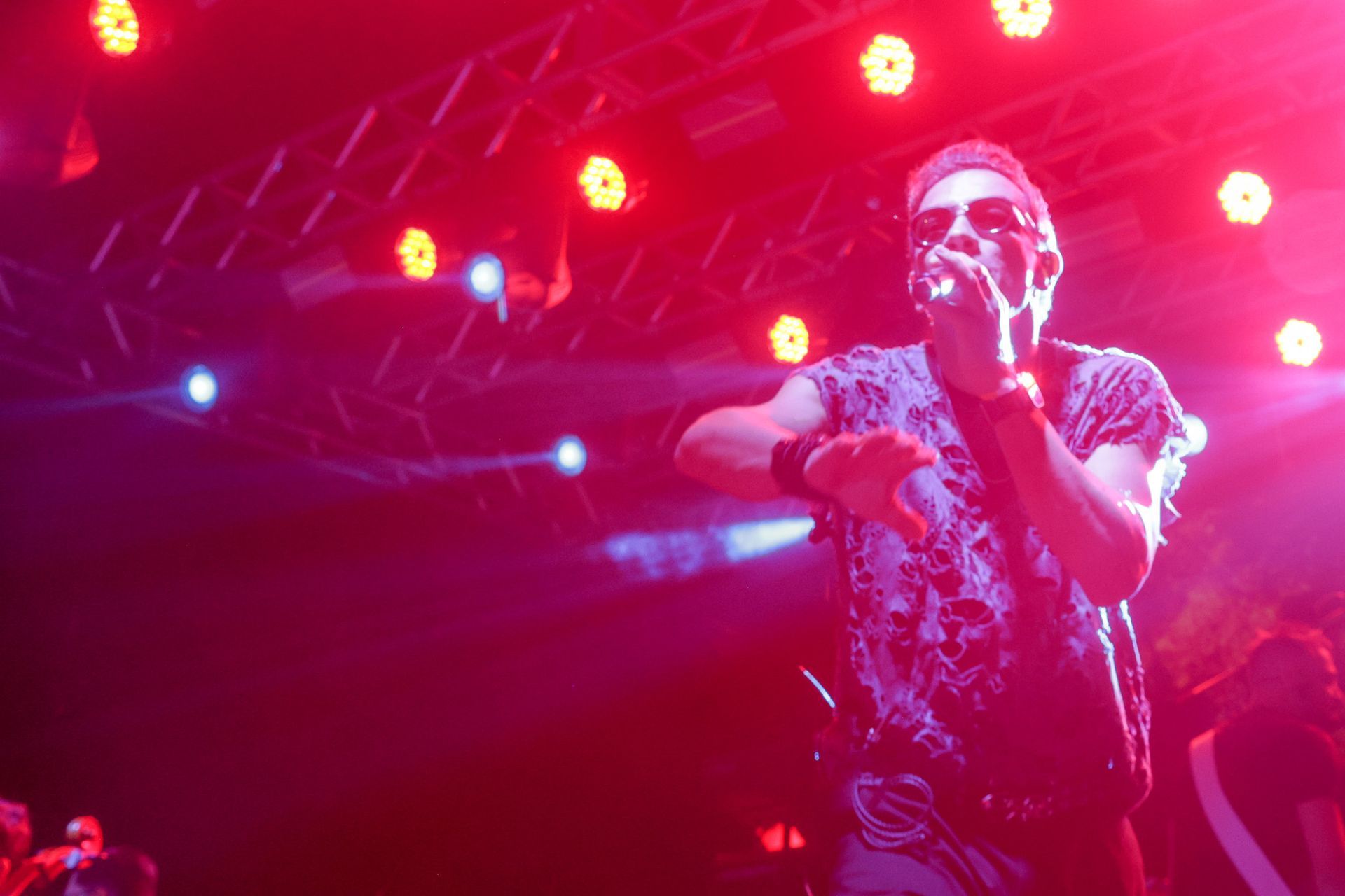 Um artista no palco, iluminado por luzes vermelhas, cantando em um microfone.