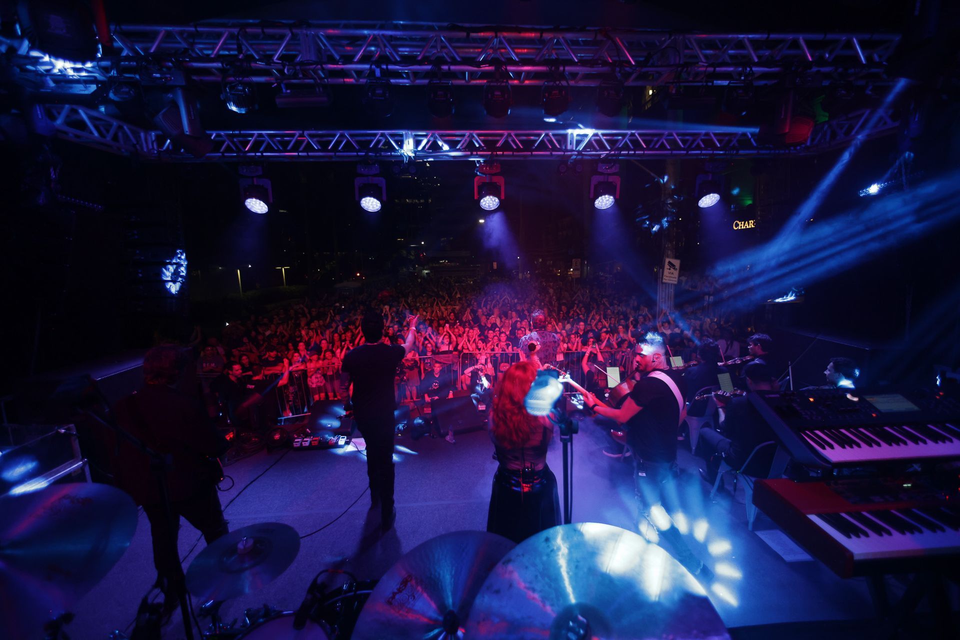 Banda se apresentando no palco sob luzes brilhantes, com uma grande multidão ao fundo.