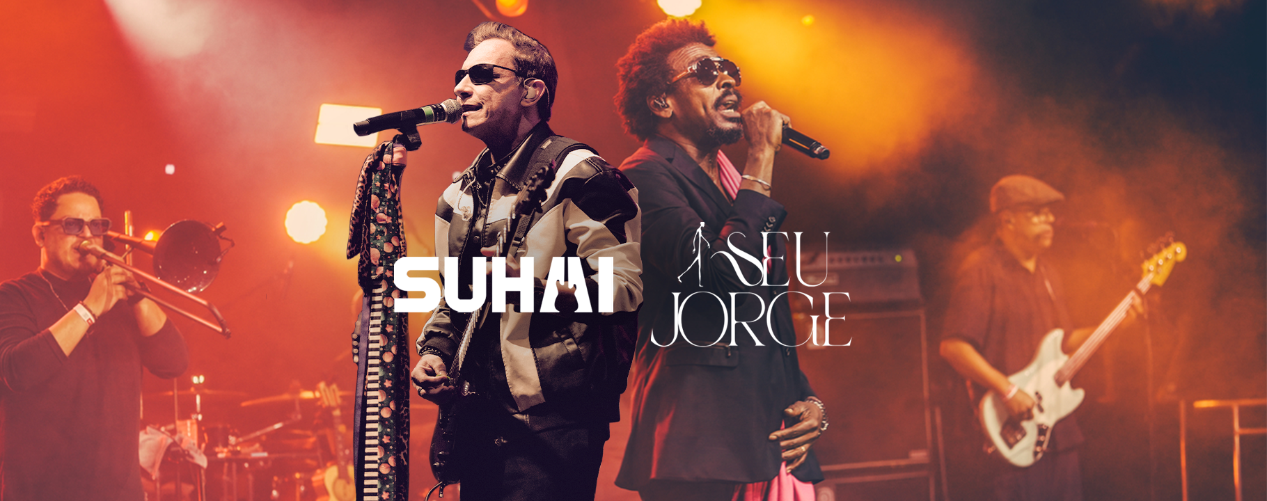 Banda se apresentando no palco com cantores e músicos, iluminados por luzes de palco laranja.