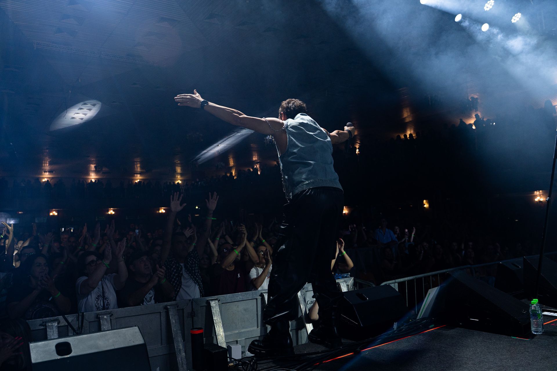 Um artista está em um palco de concerto com os braços estendidos em direção a uma plateia animada