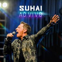 Cantor segurando um microfone no palco com a inscrição “Suhai Ao Vivo” e luzes azul-púrpura ao fundo.